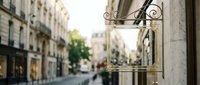 Ornate vintage street lamp with decorative ironwork hanging from historic building wall on charming cobblestone street with blurred urban background.