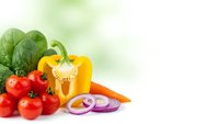 Fresh colorful vegetables including red tomatoes, yellow bell pepper, green spinach leaves and purple onion rings on white surface with soft green background.