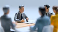 Business professionals in formal attire gathered around conference table for corporate meeting, discussing strategy and collaboration in office setting.