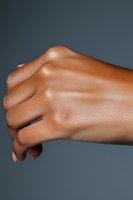 Close-up of African American woman's hand showing natural skin texture and knuckle details against dark gray background, suitable for beauty and skincare marketing.