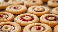 Homemade butter cookies with red jam filling and white chocolate center arranged in rows, fresh baked traditional holiday treats on light background.