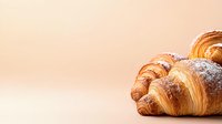 Fresh baked croissants dusted with powdered sugar on peach colored background, selective focus with copy space for menu or bakery promotion.