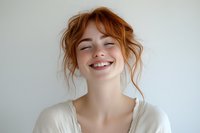 Young redhead woman with freckles and natural makeup expressing pure joy and happiness with closed eyes and genuine smile against light background.