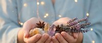Woman holding aromatic spices and dried lavender flowers in cupped hands with warm bokeh lights creating cozy atmosphere for wellness and natural remedies.
