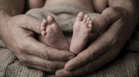 Newborn baby feet cradled in parent's hands, wrapped in soft knit blanket, capturing tender family bonding moment for parenting, healthcare, and maternity content.