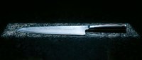 Sharp kitchen knife with black handle on dark granite countertop surface for culinary cooking and food preparation in modern kitchen setting.