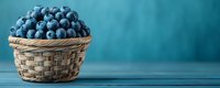 Fresh ripe blueberries in woven wicker basket against turquoise blue background on wooden table, panoramic banner format with copy space.
