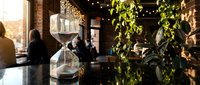 Modern restaurant interior with geometric glass vases and fresh greenery on dark table, warm ambient lighting creating cozy dining atmosphere.