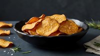 Crispy sweet potato chips in a dark ceramic bowl with sea salt and rosemary on a slate background, healthy snack concept.
