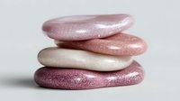 Stack of smooth, shimmering pink and cream pebbles with glitter effect on white background, creating zen-like balance for spa and wellness concepts.
