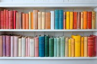 Colorful vintage books arranged in rainbow order on white wooden shelves, creating an aesthetically pleasing gradient from red through yellow, perfect for library decor.