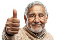 Senior Hispanic man with gray beard wearing beige sweater showing thumbs up gesture with confident smile against white background for wellness and aging concepts.