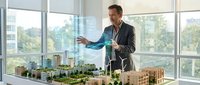 Professional architect presenting urban development model in modern office with city view through large windows.