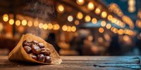 Roasted chestnuts in paper cone on wooden table with festive bokeh lights in background, creating warm holiday atmosphere.
