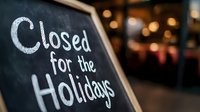 Handwritten chalk message on blackboard announcing holiday closure with blurred festive lights and decorations in background, creating warm atmosphere.