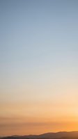 Soft gradient sky transitioning from blue to warm orange hues over mountain silhouettes at sunset creating peaceful atmospheric backdrop.