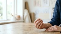 Mature man with light skin tone wearing dark blue shirt rests hands on wooden table in bright studio or office workspace, suitable for business, professional, and lifestyle editorial content.