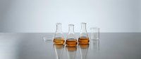 Laboratory glassware with amber liquid samples arranged on reflective surface for scientific research, chemistry education, and pharmaceutical testing applications.