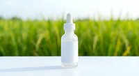 White dropper bottle with pipette on clean surface against blurred green field background for natural skincare and wellness product mockup.