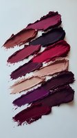 Smeared lipstick swatches in various shades of burgundy, purple, and nude pink on white background, showing texture and pigmentation of cosmetic products.