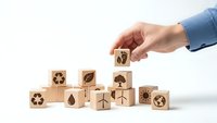 Hand placing wooden cube with eco symbols among blocks featuring recycling and environmental icons on white background for sustainable business concepts.
