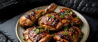 Grilled chicken thighs with teriyaki glaze and sesame seeds garnished with green onions on rustic plate for culinary marketing and restaurant menus.