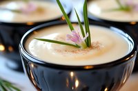 Creamy vichyssoise soup garnished with fresh chives and delicate pink flower in elegant dark bowl, soft focus background creates luxurious dining atmosphere.