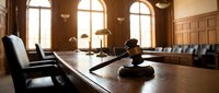 Wooden gavel on polished table in elegant courtroom with warm sunlight streaming through arched windows creating professional legal atmosphere.