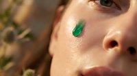 Young woman applying green skincare serum drop on face for natural beauty routine and healthy glowing skin care treatment in sunlight.