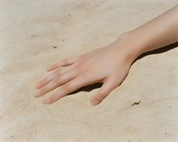 Young woman's hand touching warm golden sand on a sunny beach, feeling the texture of summer nature outdoors.