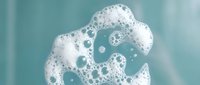 White foam bubbles floating on turquoise water surface creating abstract aquatic texture for spa wellness and cleaning product designs.