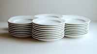 Stacks of clean white ceramic plates with minimalist design against neutral background, showcasing modern tableware essentials for food service and home dining.