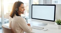 Smiling young woman customer service representative with headset working at computer in modern office environment for business communication.