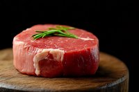 Raw beef tenderloin steak garnished with fresh rosemary on wooden cutting board against dark background, close up view showing meat texture and marbling.