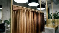 Hair extensions display in professional salon showcasing various blonde and brown shades hanging on rack for beauty treatments and styling services.