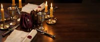 Vintage writing desk with quill pen, inkwell, sealed letters, burning candles and wine glasses creating atmospheric medieval or historical workspace ambiance.