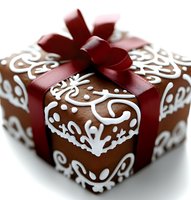 Elegantly wrapped brown gift box decorated with white ornate swirls and flourishes, topped with deep red satin ribbon bow. Festive holiday or special occasion packaging.