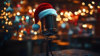 Vintage microphone wearing red Santa hat against blurred Christmas lights background, creating festive holiday atmosphere for music performance.