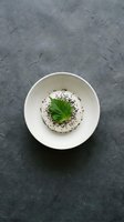 White ceramic bowl with green leaf and black sesame seeds on dark slate surface for culinary presentation and food styling projects.