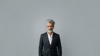 Mature male professional with gray hair and beard wearing dark blazer and white shirt against neutral gray background for corporate portraits.