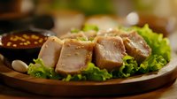 Juicy sliced chicken breast fillet on fresh green lettuce leaves served on wooden plate with soy sauce and garlic cloves, restaurant food styling.