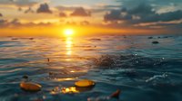 Dramatic ocean sunset with golden sun reflecting on rippling water surface and floating pebbles, creating tranquil seascape with deep blue and orange colors.