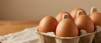 Fresh brown chicken eggs in cardboard carton on wooden table with natural lighting for cooking and baking ingredients in kitchen setting.