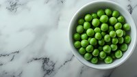 Fresh green peas in white ceramic bowl on marble background with copy space. Top view of healthy organic vegetables for cooking and nutrition.