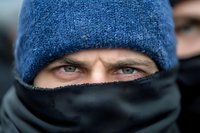 Man in blue knit hat and black face mask with intense eyes looking directly at camera during cold weather outdoor winter portrait.