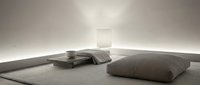 Minimalist bedroom interior with low platform bed and floor cushion in neutral tones. Modern zen-style sleeping space with clean lines and soft lighting.