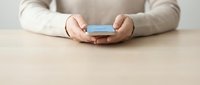 Woman hands holding smartphone on wooden table surface in minimalist setting for communication and technology concepts.