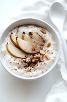 Creamy rice pudding topped with caramelized pear slices, toasted pine nuts and cinnamon dust in white ceramic bowl on light background. Perfect for dessert menu.