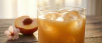 Refreshing peach iced tea in a glass with ice cubes on a rustic wooden table, with fresh peach slices and a flower in the background.