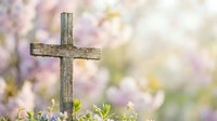 Wooden cross standing in spring garden with soft pink cherry blossoms and fresh green leaves creating peaceful Easter and faith background for religious designs.